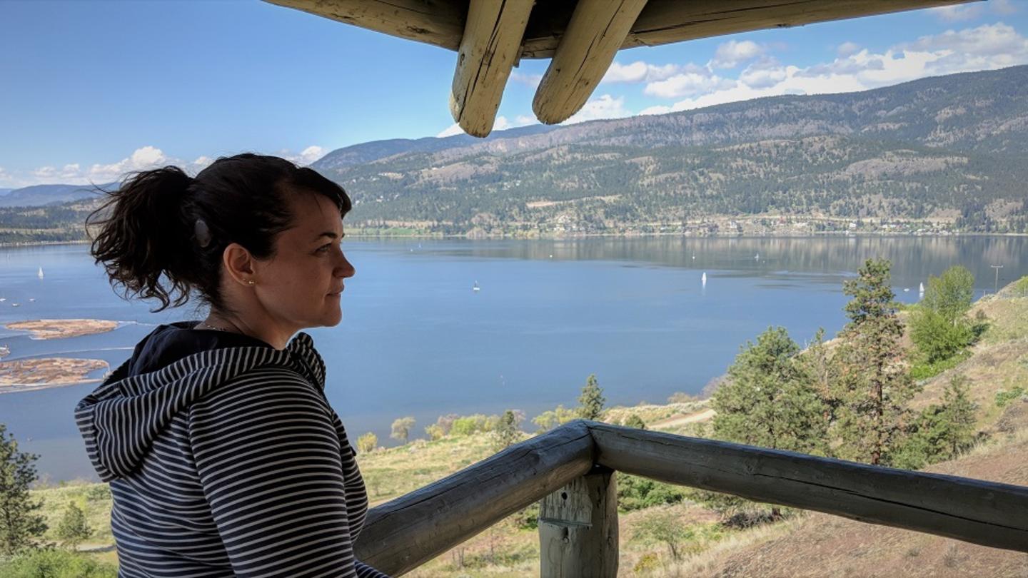 A woman with a cochlear implant stands in front a lake