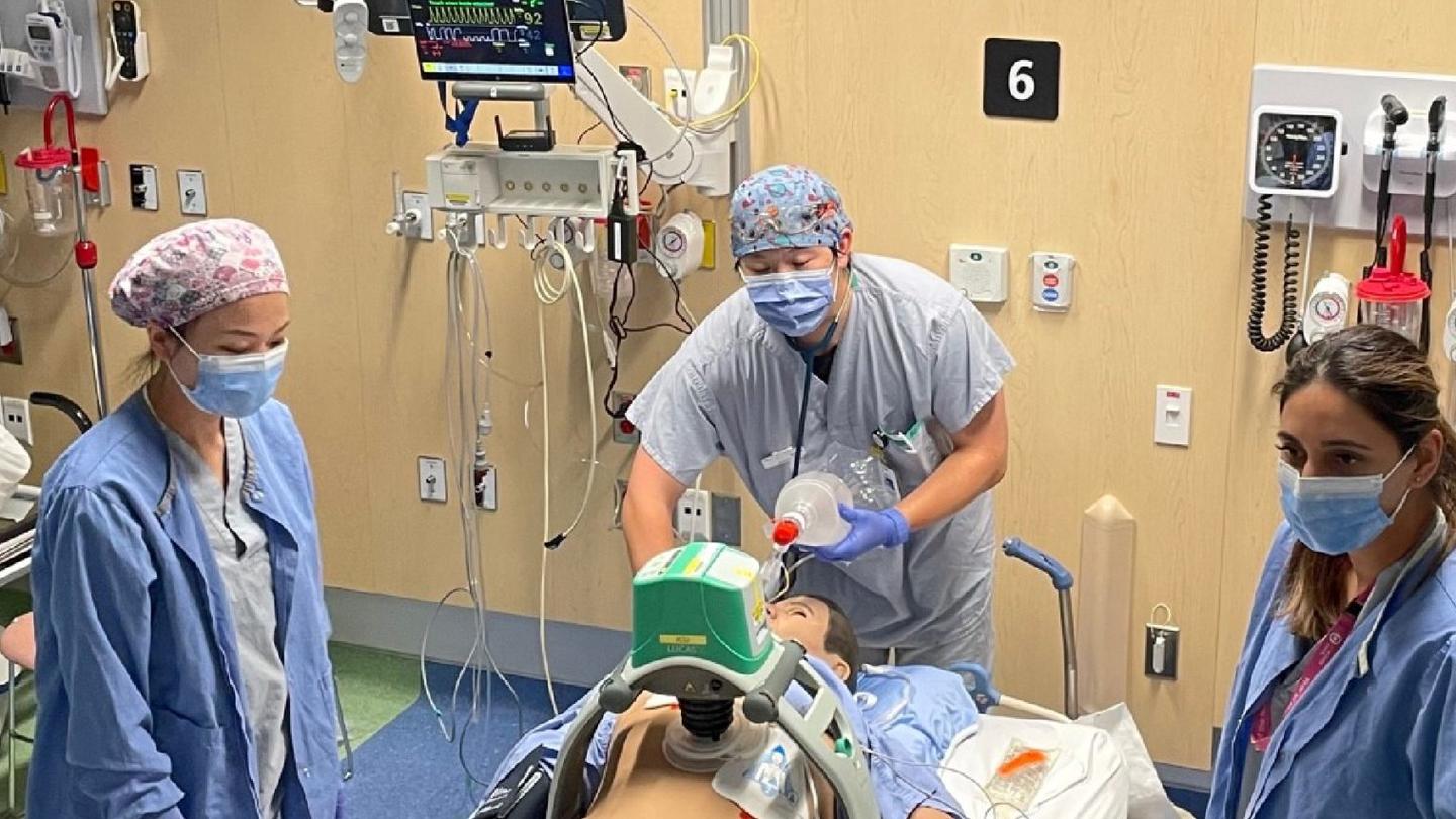 People in scrubs stand around a mannequin simulating medical care