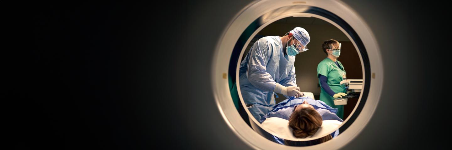 Patient lies on CT scan bed as a doctor performs a procedure on her