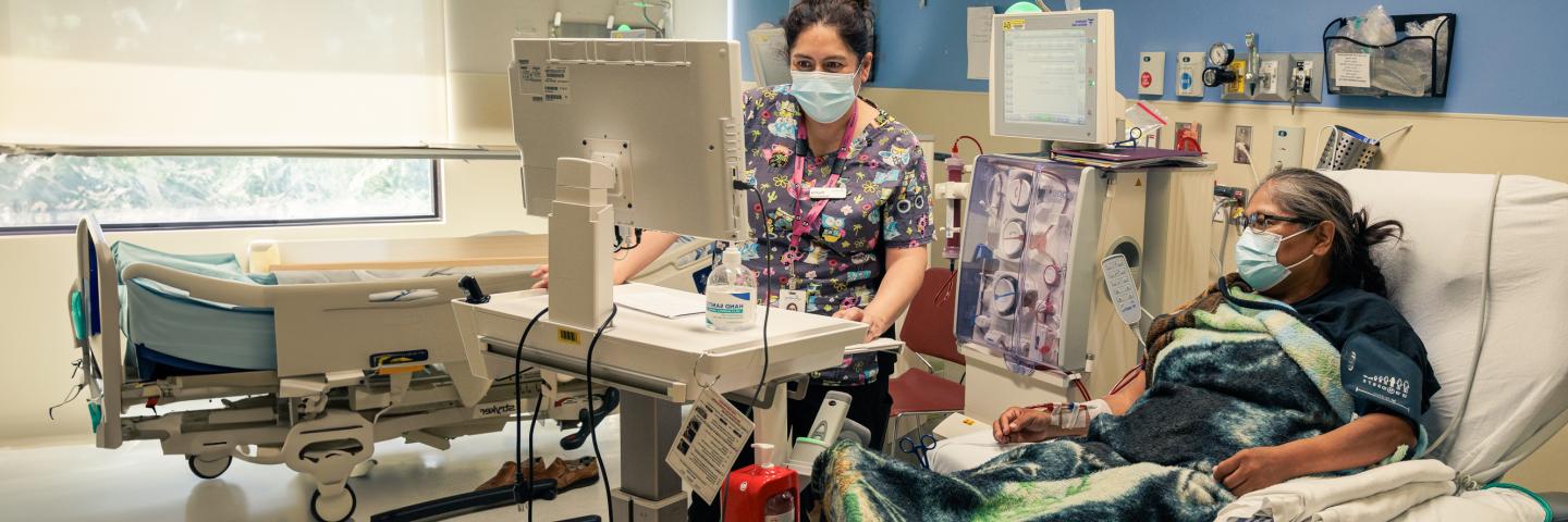 Nurse looks at her monitor as a patient lies in a bed beside her