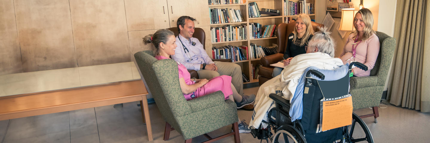 Doctors and nurses seated in a circle smile and talk to a tenant