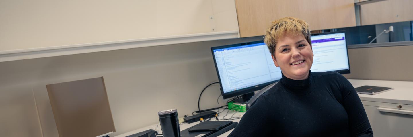 Staff member smiling in their office with two monitors behind them