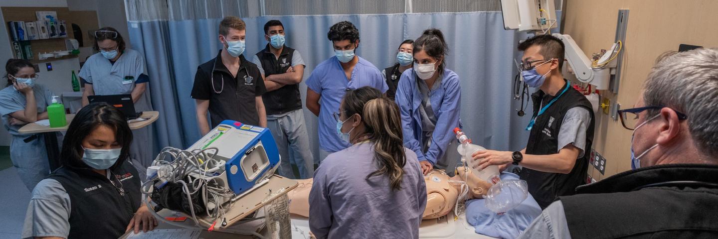 Several participants are standing around a mannequin watching an individual participant practice medical procedures