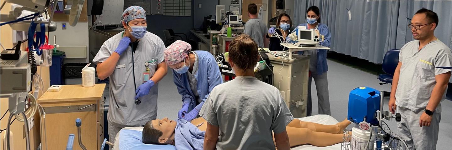 People in scrubs stand around a mannequin simulating medical care