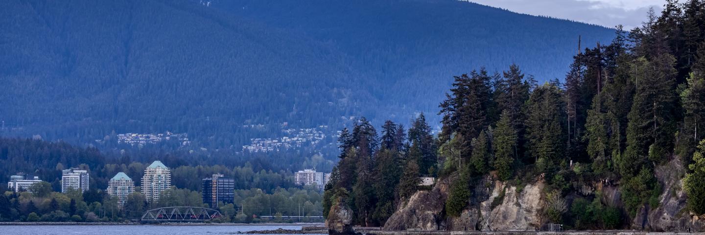 A photo of Vancouver's North Shore mountains with buildings, trees and the ocean in the foreground