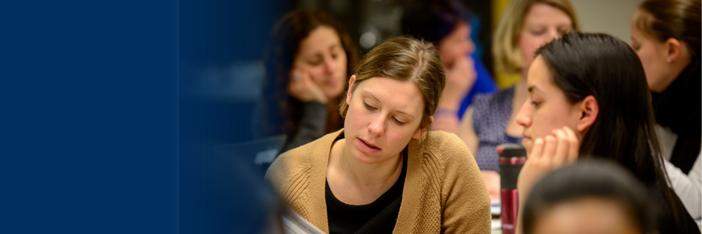 Two women sit across from each other at a desk and look at a document together