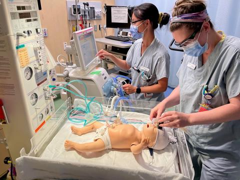 Two women in scrubs simulate care on an infant mannequin