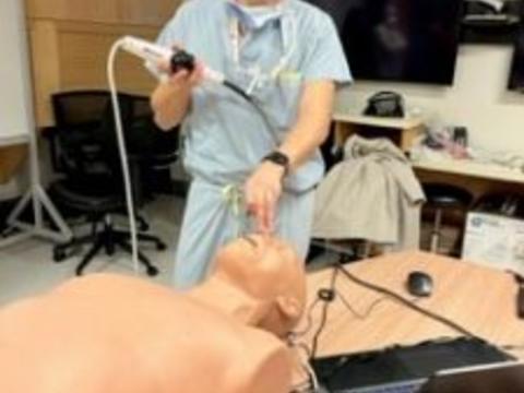 A man in scrubs uses an ultrasound on a torso mannequin