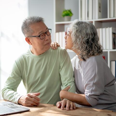 An Asian man and woman sit at a desk looking at each other with a laptop open in front of them